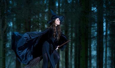 a woman dressed as a witch riding a broomstick in the woods