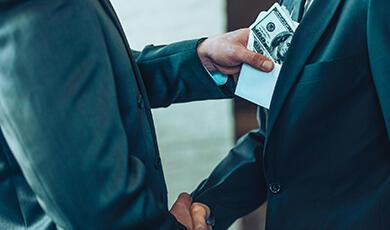 a man putting money into the inside pocket of another man while shaking his hand