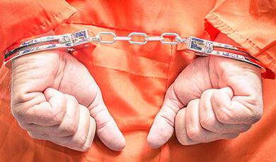 Hands in handcuffs behind the back of someone wearing an orange jumpsuit