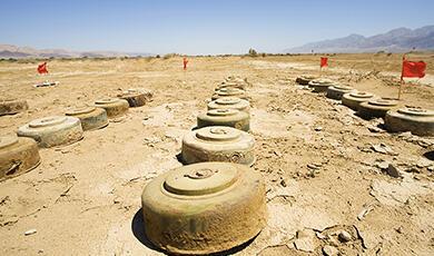 Rows of anti-tank mines in a barren desert landscape, marked by red flags