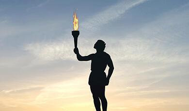 A silhouette of an athlete holding a flaming torch against a sunset sky
