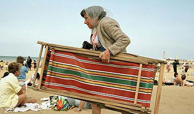 A woman carrying a striped beach chair on a crowded beach