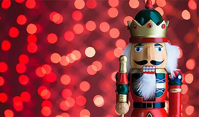 A traditional wooden nutcracker soldier stands in front of a festive red sparkly background