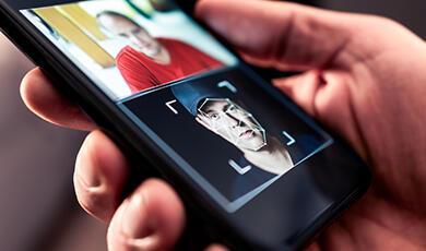 A phone screen showing facial recognition scanning a man’s face in a photo.