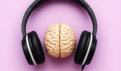 A human brain model positioned between a pair of black over-ear headphones, all set against a pink background