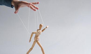 A hand manipulates a wooden puppet with strings