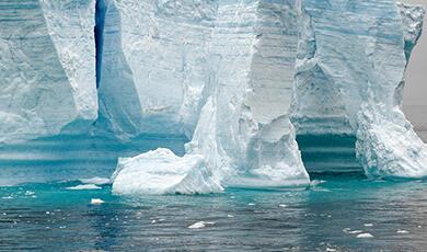 A large, textured tabular iceberg floats in blue water, with smaller ice fragments nearby