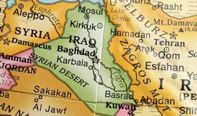 A close-up photograph of a colourful political map focusing on the Middle East, showing labelled countries including Syria, Iraq, Iran, Jordan, and Kuwait, along with major cities like Baghdad, Damascus, and Tehran