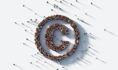 A high-angle, overhead shot shows a large crowd of people gathered on a white surface to form the shape of a copyright symbol
