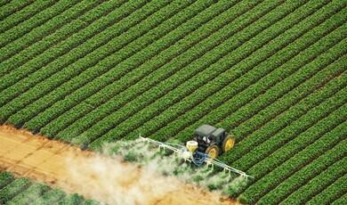 An aerial, high-angle shot shows a dark green tractor driving through a meticulously planted agricultural field