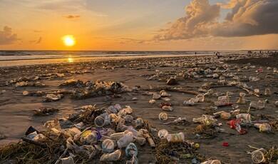 A beach at sunset covered in plastic cups, bags, and debris