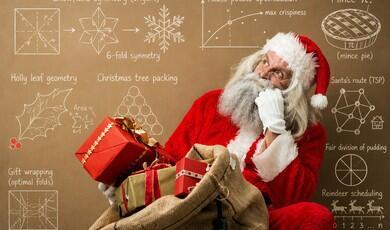 An older man dressed as Santa Claus looking thoughtfully upward while holding a large burlap sack filled with wrapped gifts. He wears a classic red and white suit, a matching hat, white gloves, and has a full white beard