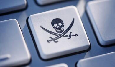 A close-up shot of a white computer keyboard key featuring a black Jolly Roger symbol, which consists of a skull over two crossed cutlass swords, surrounded by other metallic grey keys