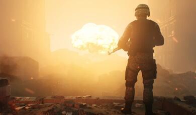 A soldier in digital camouflage uniform stands with their back to the viewer, holding a rifle and looking out over a ruined, hazy city landscape where a large explosion flares in the distance under an orange sky