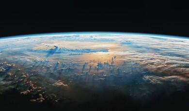 A high-angle, wide shot of Earth's curved horizon against the blackness of space. Wispy white clouds cover the landscape, casting long, dramatic shadows across a golden, sunlit ocean surface below