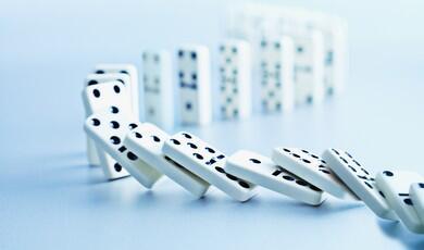 A line of white dominoes with black dots falling down in a chain reaction, curving smoothly across a light blue surface