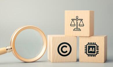 A magnifying glass with a light wood handle rests on its side on a solid grey surface. To its right, three light wood blocks are stacked in a small pyramid. The top block features a black icon of the scales of justice. The bottom-left block shows a black copyright symbol, while the bottom-right block depicts a black microchip icon enclosing the letters "AI"