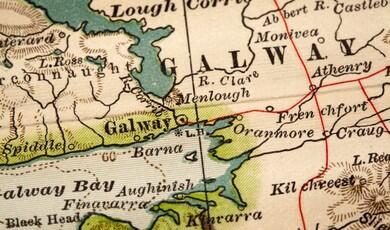 A close-up photograph of an vintage, illustrated paper map focusing on Galway, Ireland, showing coastal features, roads, and surrounding town names like Barna and Oranmore