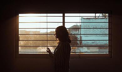 Woman in dark room looking out through blinds