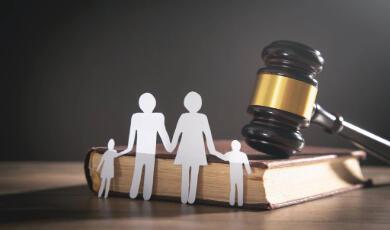 Paper cut outs of woman, man and two children in front of a gavel and book
