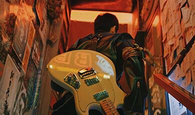 man carrying electric guitar up stairs in a club
