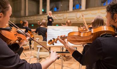 Violinists and conductor in small hall