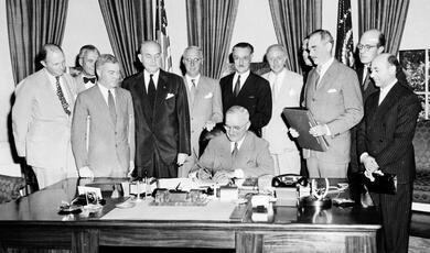 Truman signing North Atlantic Treaty in Oval Office with colleagues around him